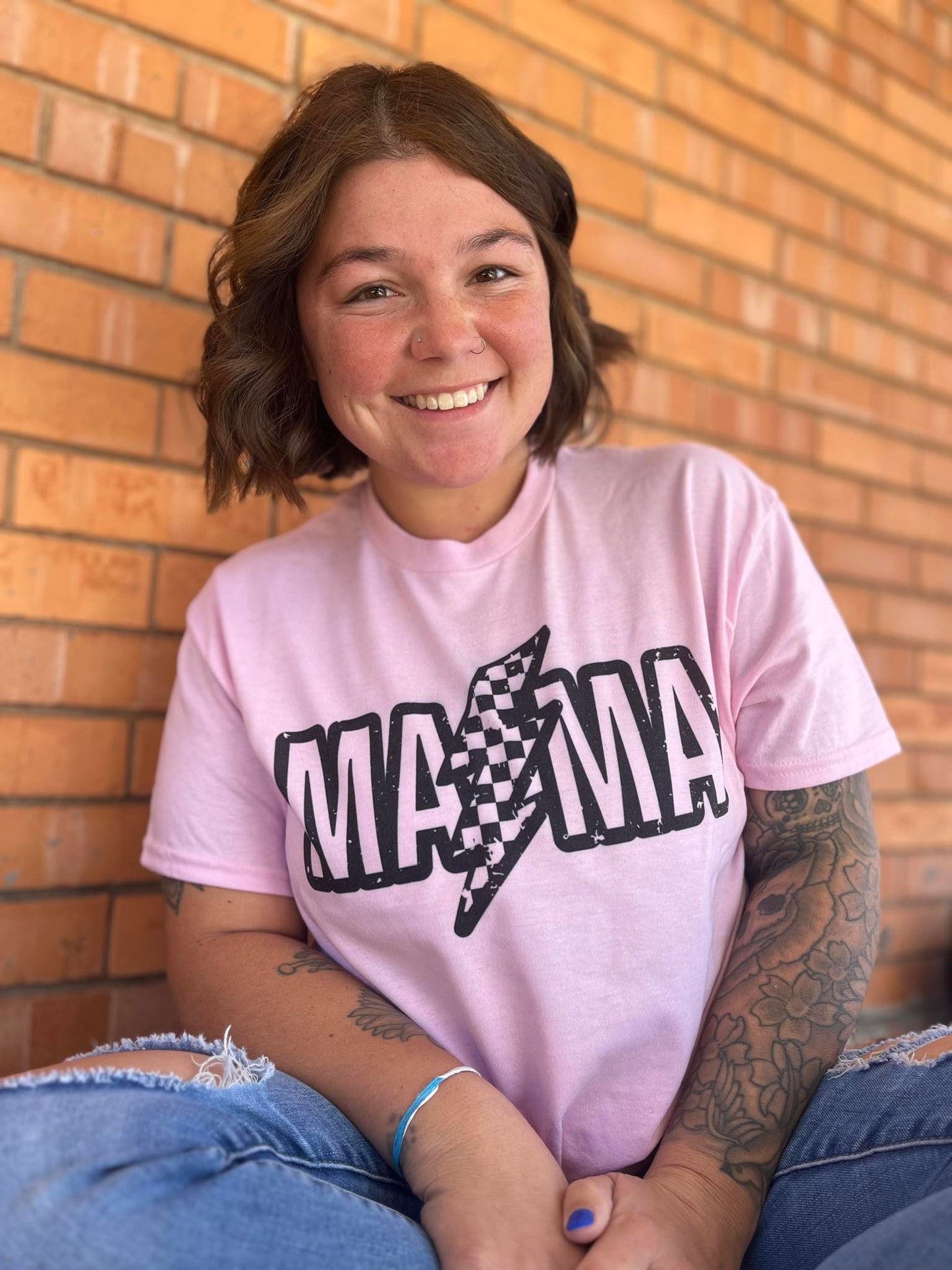 A person smiling and wearing a pink custom T-shirt with the word 'MAMA' printed in black.