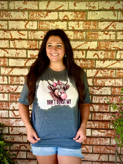 Woman wearing a graphic t-shirt with a cow design and text, standing against a brick wall.