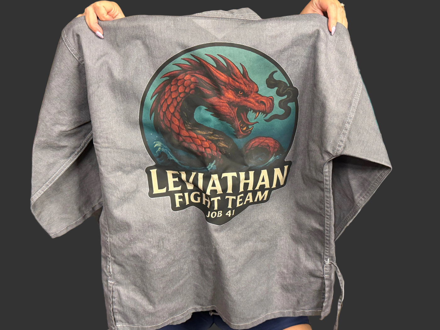 Gray karate shirt with Leviathan Fight Team logo held up in a casual setting
