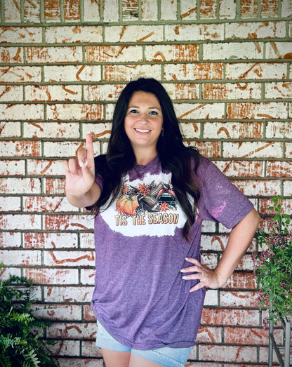 Woman wearing a purple t-shirt with a graphic design in front of a brick wall.